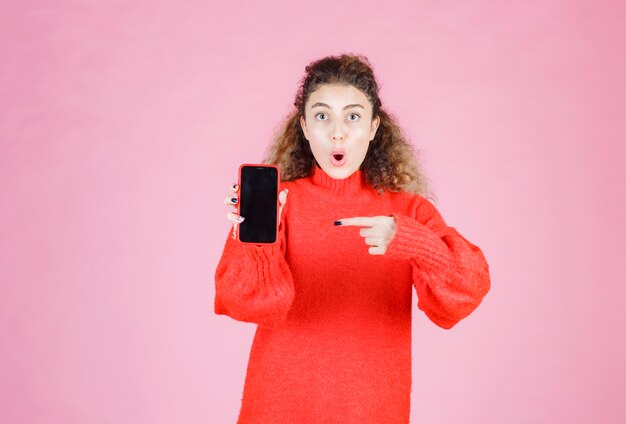 彼女の新しいブランドのスマートフォンを持って指さしている女性。