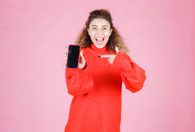 彼女の新しいブランドのスマートフォンを持って指さしている女性。