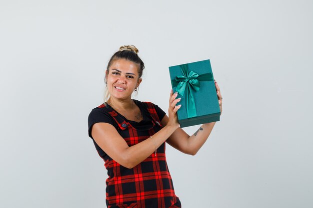 Woman holding present box in pinafore dress and looking cheerful , front view.