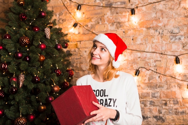 Woman holding present next to christmas tree