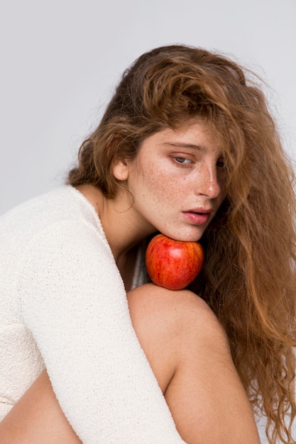 Woman holding a red apple between her face and knee