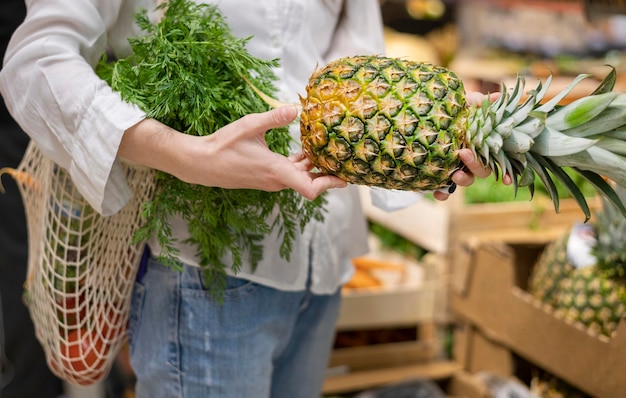 Woman holding reusable bag and pineapple in grocery store