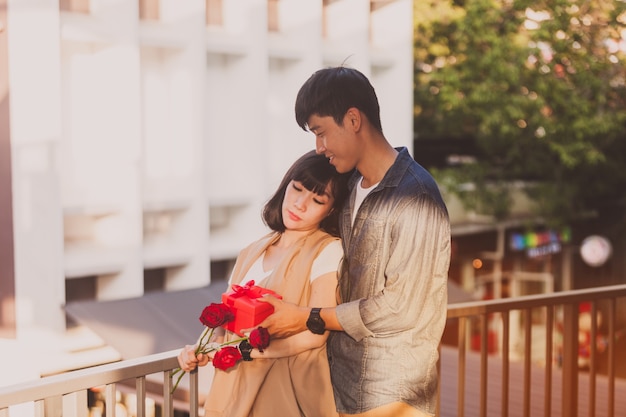 Woman holding roses while her boyfriend gives her a gift box