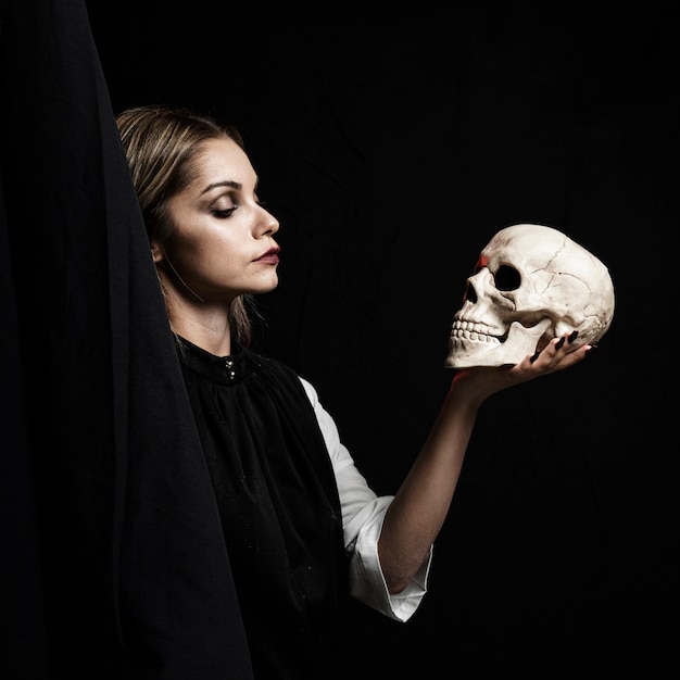 Woman holding skull on black background