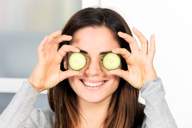 Woman holding slice of cucumber over eye