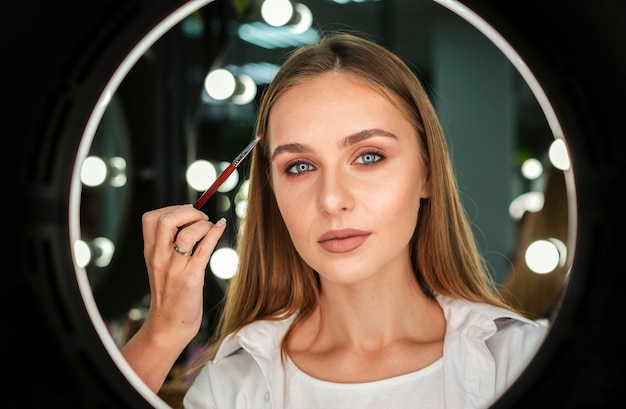 Woman holding small brush looking at mirror