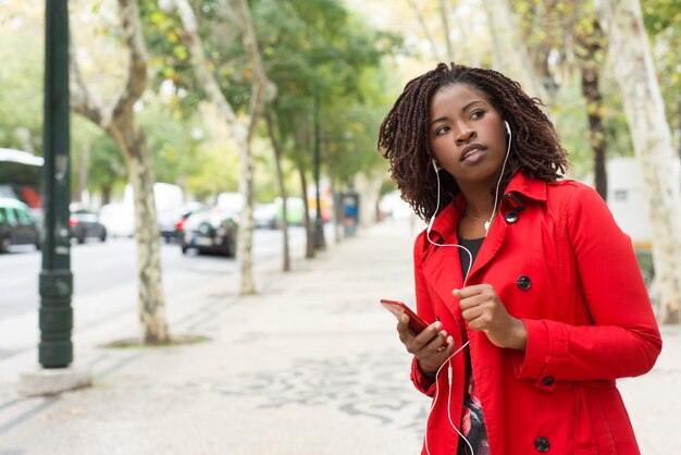 Женщина держит смартфон и смотрит в сторону на улице