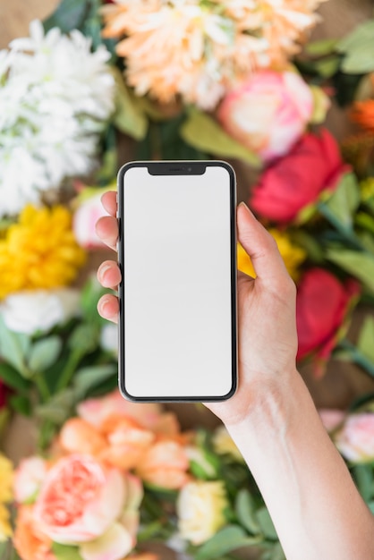 Free photo woman holding smartphone with blank screen above flowers
