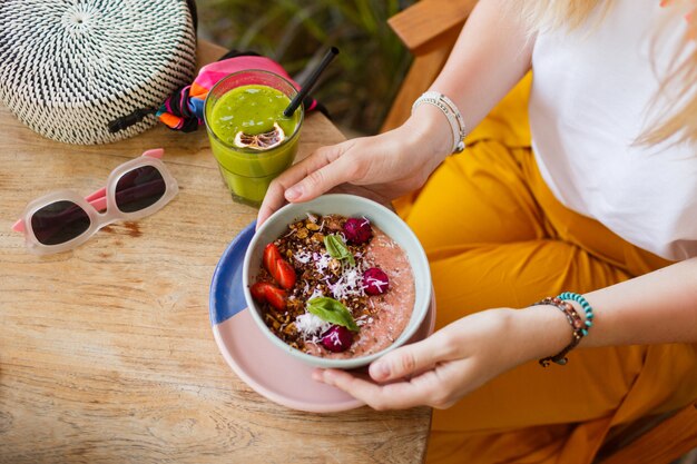 Woman holding smoothie. Superfoods bowl topped with chia, granola and avocado.