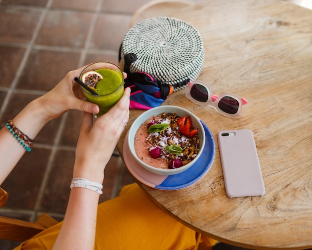 Woman holding smoothie. Superfoods bowl topped with chia, granola and avocado.