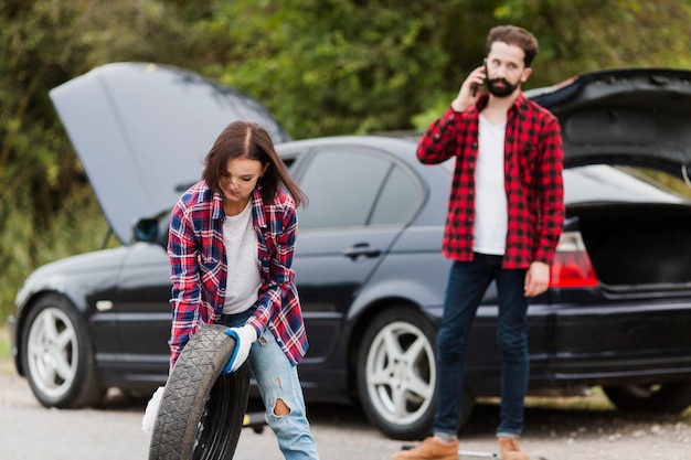 Woman holding spare tire and man talking on phone