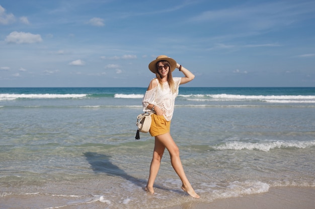 Женщина держит соломенную сумку и гуляет по пляжу