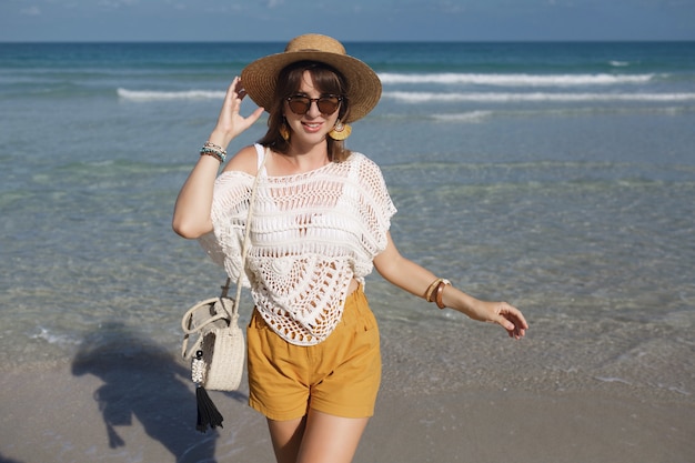 Free photo woman holding straw bag and walking on the beach