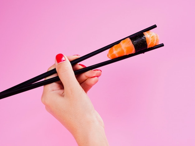 Woman holding sushi in chopsticks on rose background