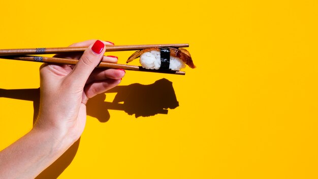 Woman holding a sushi in chopsticks on yellow background
