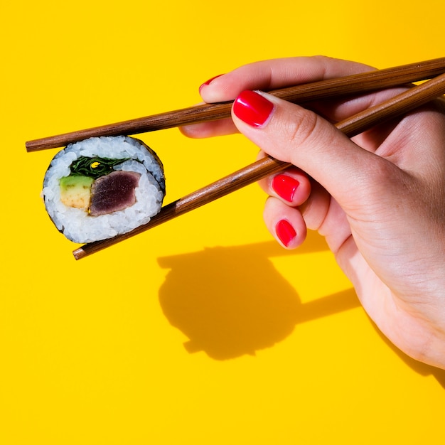 Woman holding a sushi roll in chopsticks on yellow background