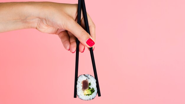 Woman holding a sushi roll on a rose background