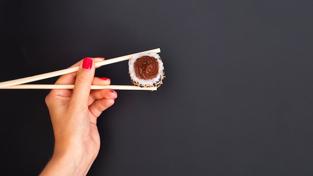 Free photo woman holding a sushi roll with chopsticks on a grey backgrund