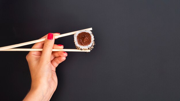 Woman holding a sushi roll with chopsticks on a grey backgrund