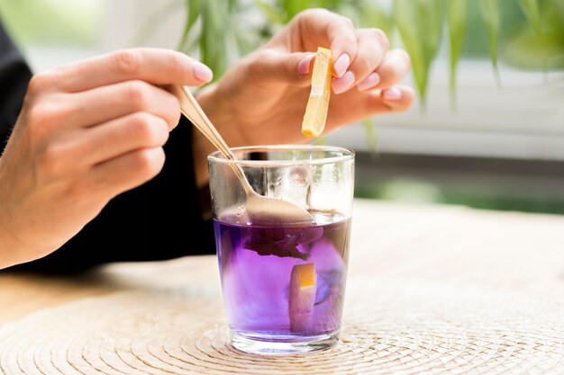 Woman holding teaspoon and lemon slice over purple tea