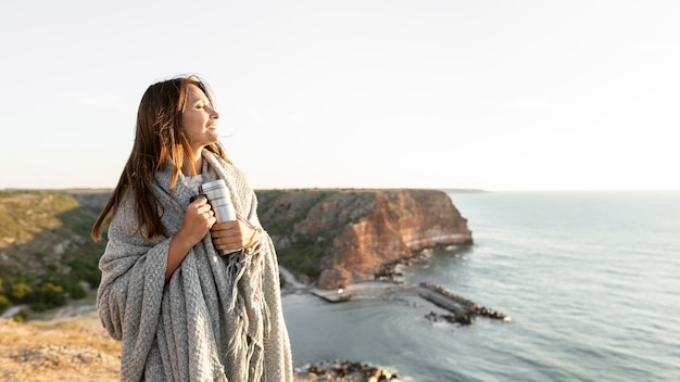 Woman holding a thermos while walking on a coast with copy space