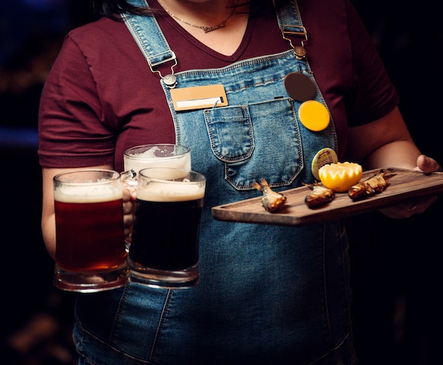 Woman holding three beer mugs and platter of smoked fish with lemon