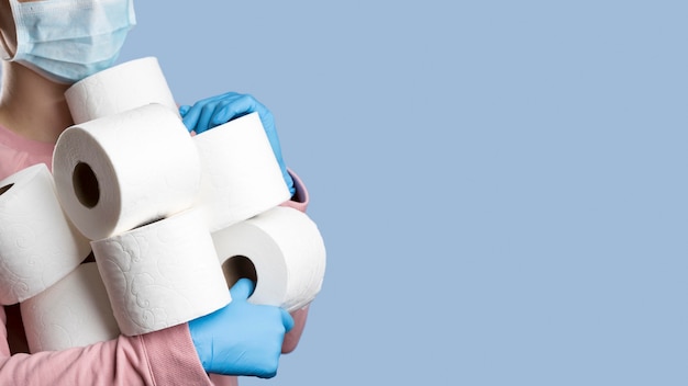 Woman holding toilet paper rolls while wearing surgical gloves and medical mask