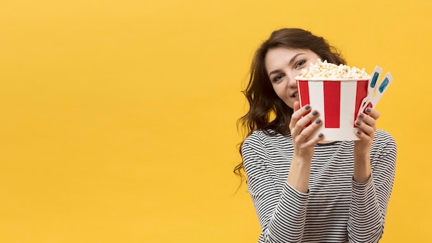 Женщина держит в руках 3D-очки и ведро с попкорном