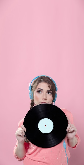 Woman holding up vinyl record while wearing headphones