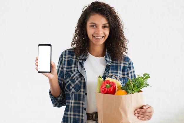 Женщина держит сумку с овощами и телефон макет