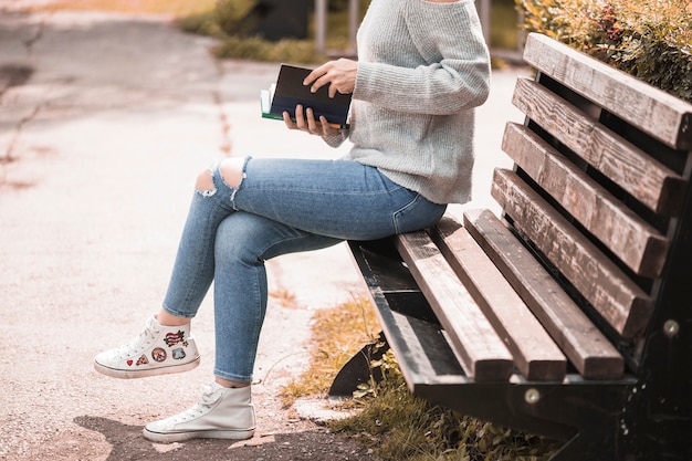 Foto gratuita donna che tiene il volume e seduto sulla panchina