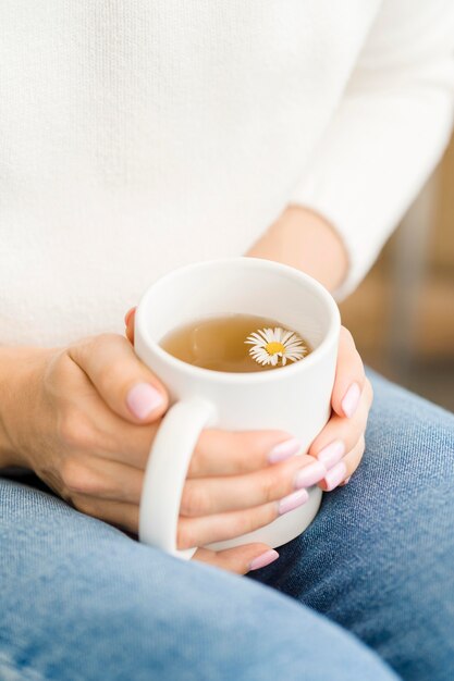 Woman holding white mug with tea and flower