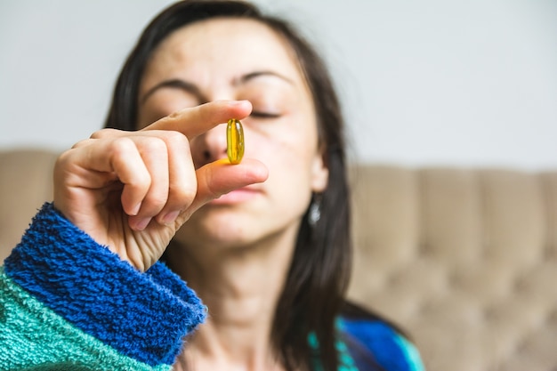 Woman holding a yellow pill in front of her face