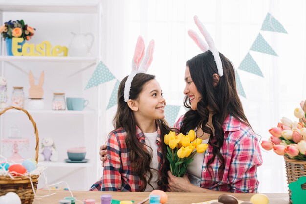 Woman holding yellow tulips bouquet embracing her daughter on easter day celebration