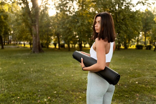 Женщина держит коврик для йоги, вид сбоку