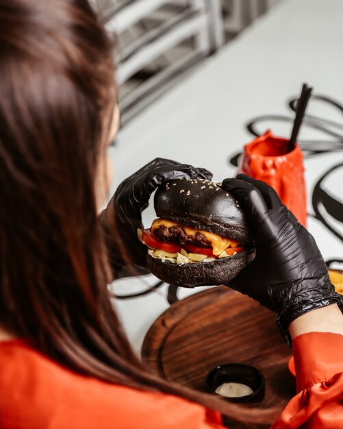 Woman holds black cheeseburger in hands