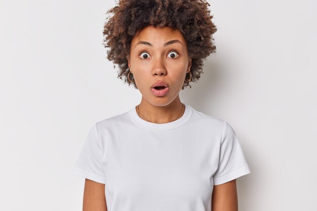 女性は息を止めて目が飛び出している衝撃的なニュースを信じることができない白いスタンドに隔離されたカジュアルなTシャツを着ているのが心配です。人間の反応の概念