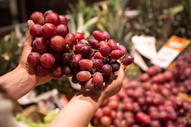 The woman holds bunch of grapes in the store or in the market close up