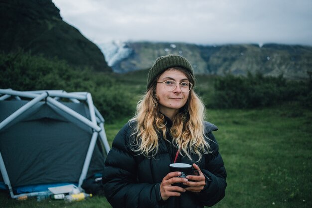 여자는 아이슬란드에서 하이킹 여행에 캠핑 찻잔을 보유