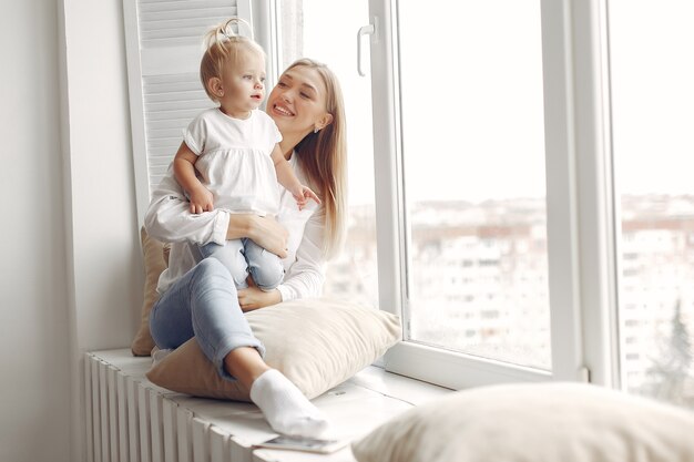 女性は子供を腕に抱き、抱きしめます。白いシャツを着たお母さんが娘と遊んでいます。家族は週末に楽しんでいます。