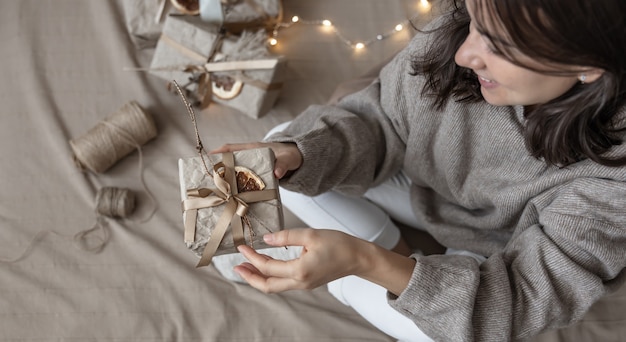 A woman holds a Christmas gift box decorated in craft style, decorated with dried flowers and a dry orange, wrapped in craft paper.