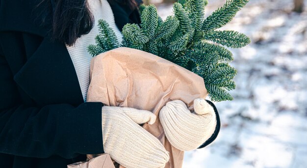 冬の森でクリスマスツリーの枝が入ったクラフトバッグを持つ女性