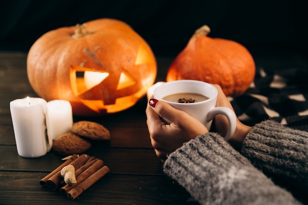 Woman holds a cup of hot chocolate in her arms before a halloween pumpkin