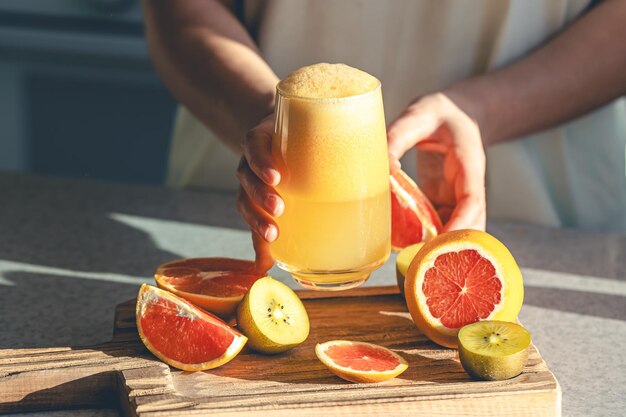 A woman holds a glass of freshly squeezed juice in her hands in the kitchen