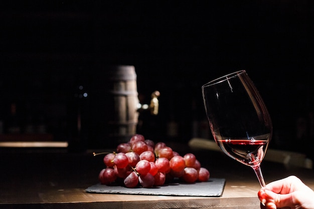 Женщина держит бокал вина перед гроздью винограда, лежащего на черной пластине