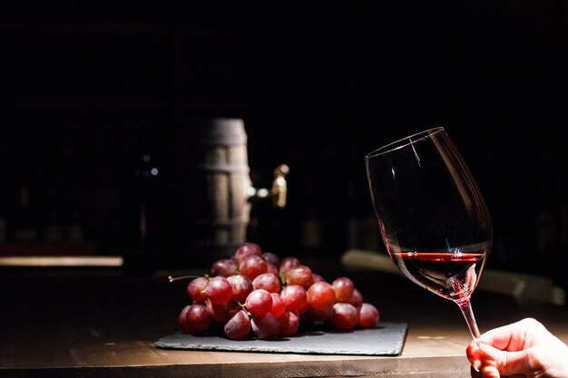 Женщина держит бокал вина перед гроздью винограда, лежащего на черной пластине