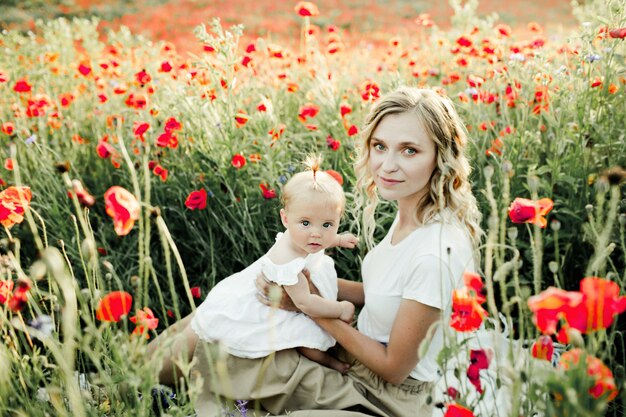 Woman holds her baby among poppy field