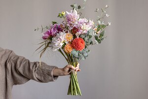 Foto gratuita una donna tiene in mano una composizione floreale festiva con fiori di crisantemo luminosi, un bouquet festivo.
