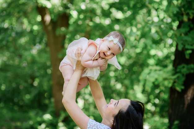 Woman holds her little daughter up standing in a green forest