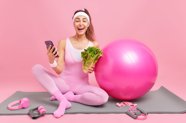 無料写真 女性は携帯電話を持って、ワークアウト中に消費したカロリーがアクティブで健康的なライフスタイルを導き、緑を食べ続け、スポーツ用品を備えたマットの上に座って食事をします。